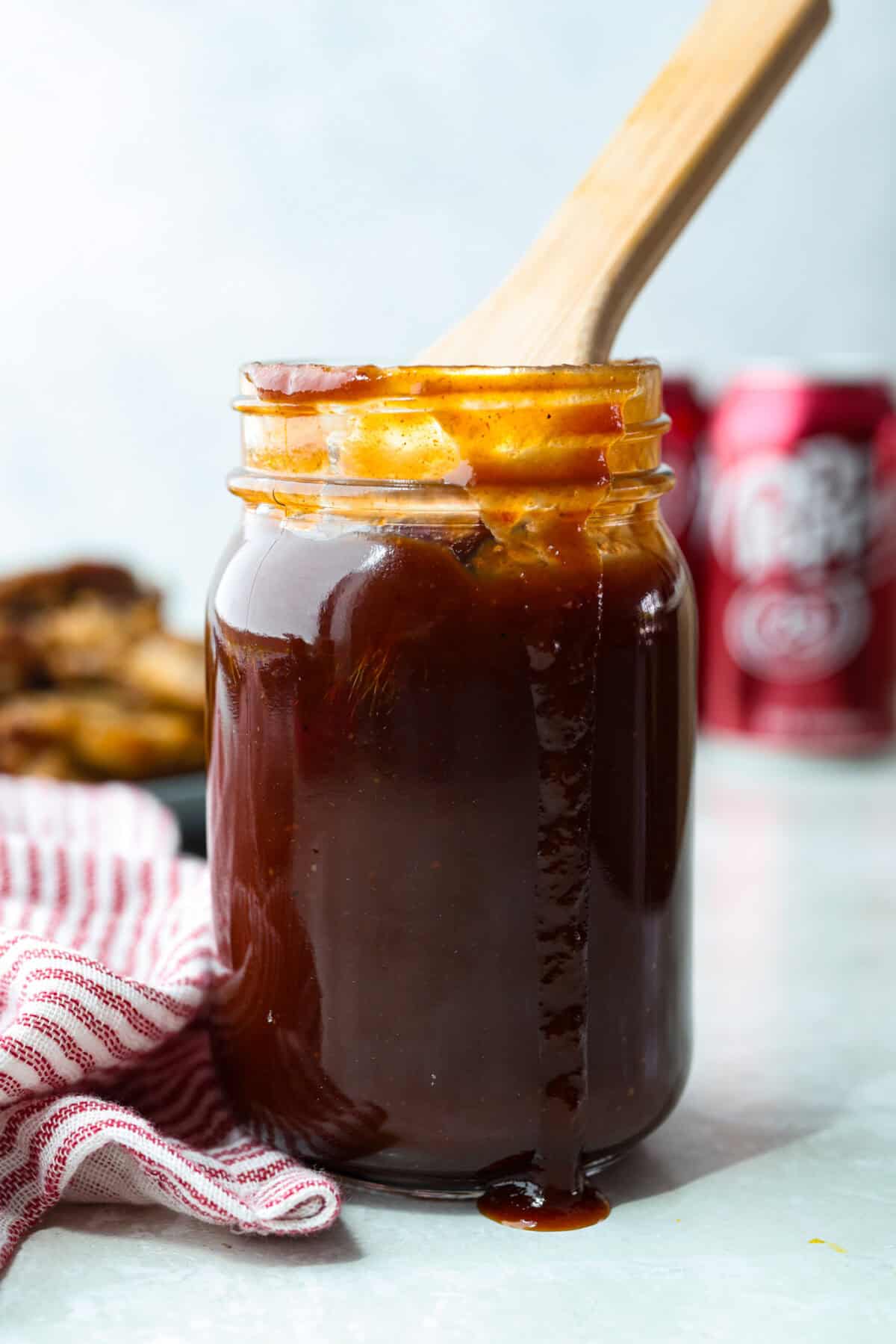 My Dr Pepper BBQ sauce is sweet, tangy, smoky, and seriously addictive! Made with simple ingredients and Dr Pepper for aย rich caramelized flavor. Itโs perfect for all your BBQ sauce needs! Bottle of Dr Pepper BBQ sauce with a wooden spoon sticking out of it, and cans of Dr Pepper in the background.