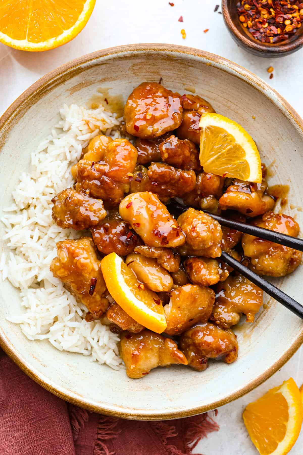 Skip the drive-thru and make this copycat Panda Express orange chicken at home! Crispy chicken coated in a sweet, sticky orange sauce with a secret ingredient that makes it taste just like the real thing. Perfect for an easy takeout-style dinner the whole family will love. Plated Panda Express Orange chicken on a bed of white rice.