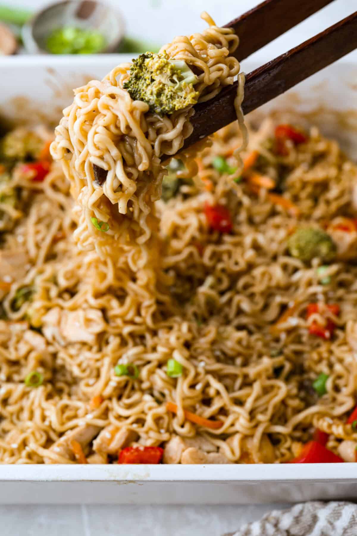 I kept seeing this dump and bake ramen all over my feed and finally had to try it for myself! Turning family favorite ramen into a cozy baked dinner was an immediate hit! It's so good with tender noodles, colorful veggies, and a savory sauce! Someone lifting a bite of dump and bake ramen out of the baking dish with chopsticks.