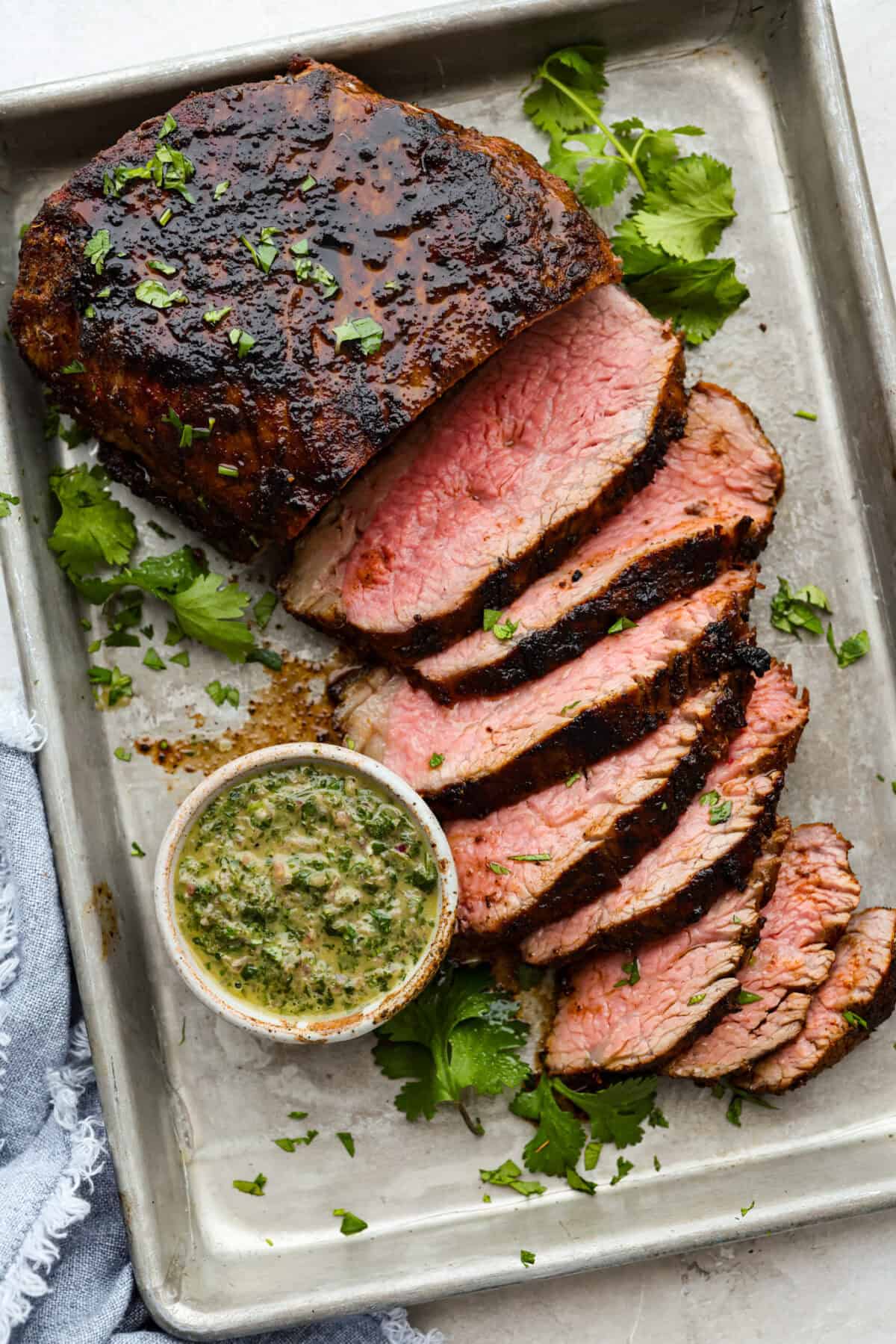 Santa Maria grilled tri-tip is juicy, smoky, and loaded with bold flavor from a delicious spice rub. Grilled until perfectly tender with a gorgeous crust, itโs an easy recipe thatโs always a hit at cookouts and summer dinners. Sant Maria grilled tri-tip sliced on a baking sheet next to a small bowl of fresh chimichurri sauce.