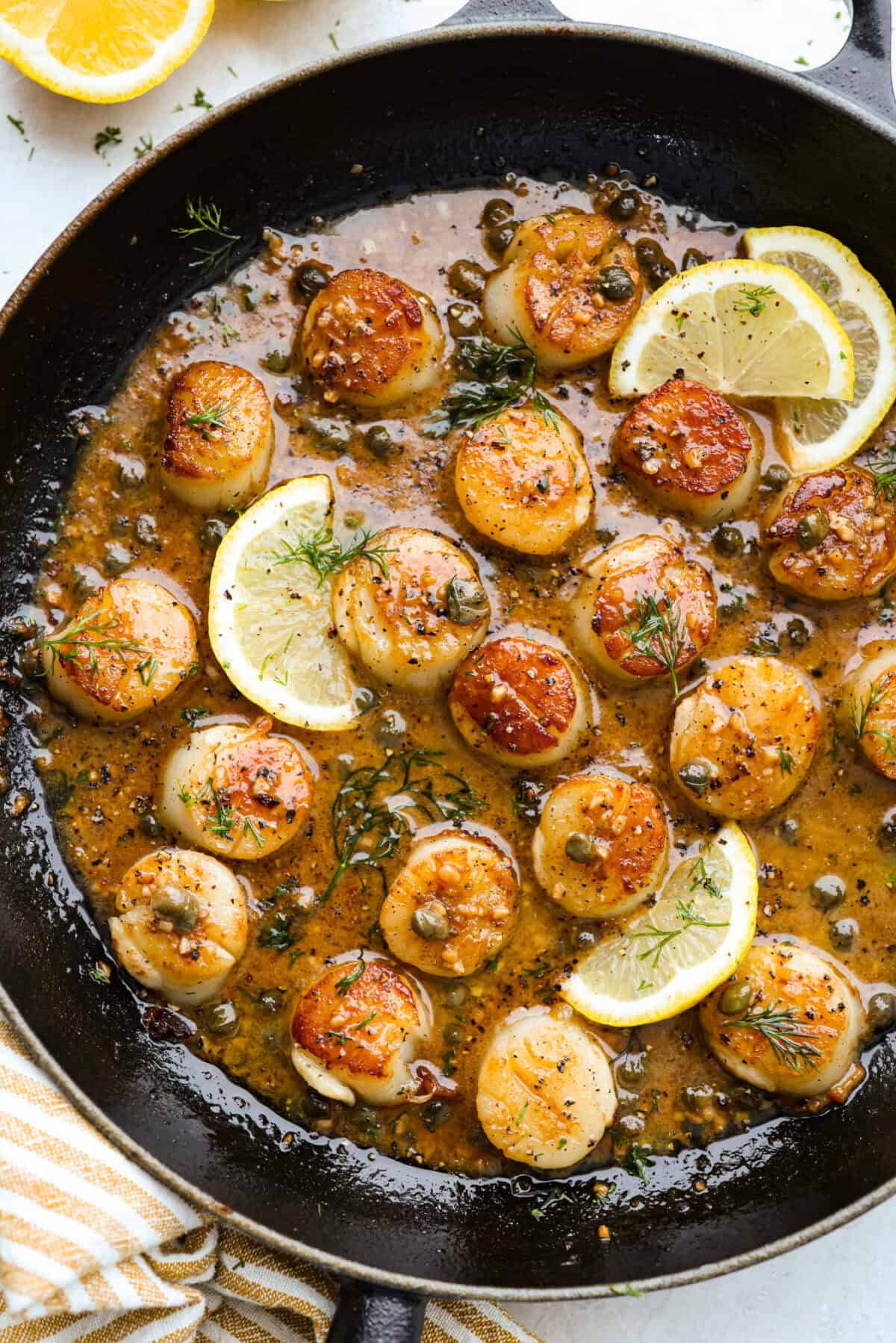 My pan seared scallops recipe has been a reader favorite for years, and one bite will show you why. The buttery golden scallops with that bright, fresh lemon flavor are what make this recipe stand out from all the others. Skillet lemon wedges and pan seared scallops in a caper sauce.