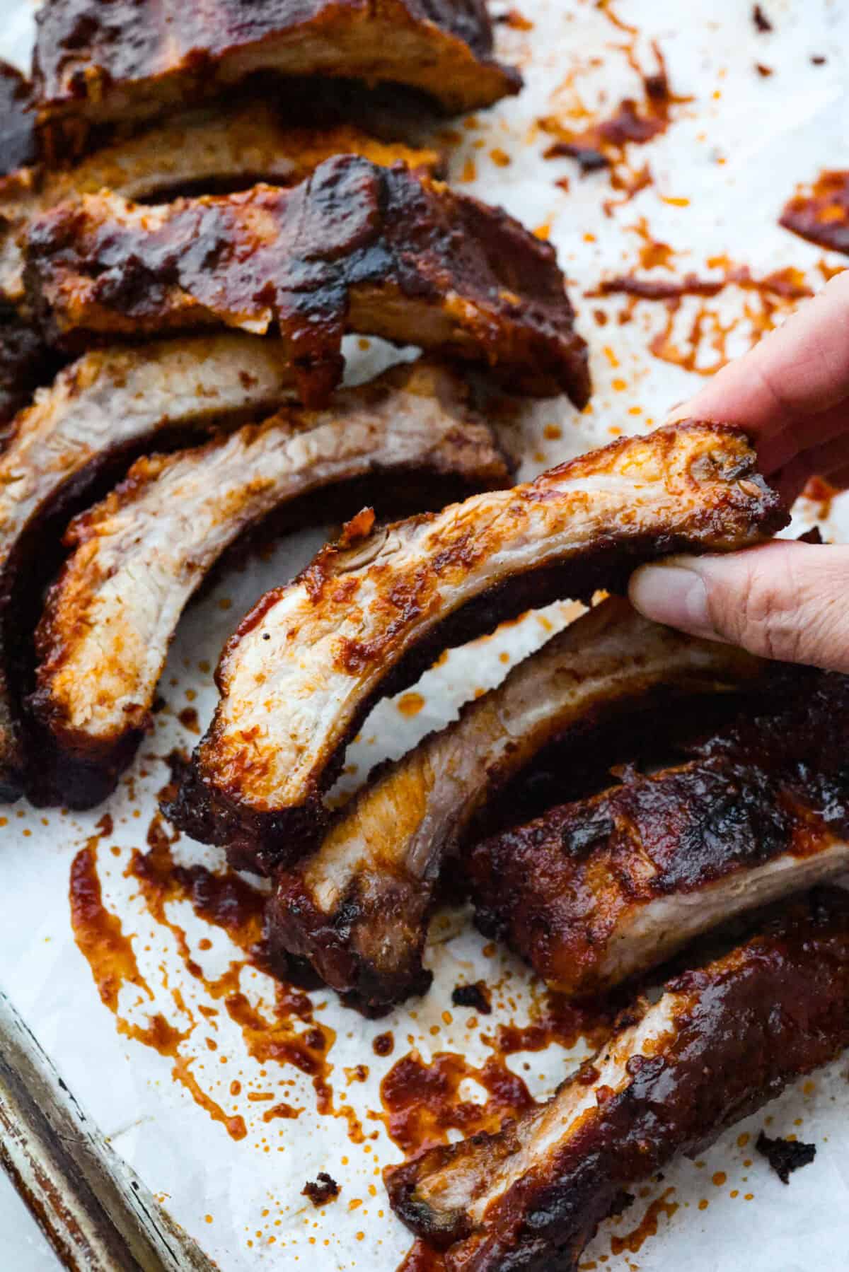 These grilled BBQ ribs are what summer cookouts are all about! Slow-cooked until fall-off-the-bone tender, then finished with a sticky, caramelized layer of BBQ sauce that'll have everyone licking their fingers. Someone picking up a grilled bbq rib/