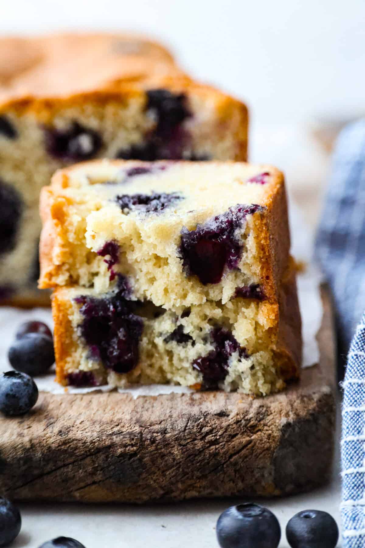 This 5 Ingredient Blueberry Bread is the little shortcut loaf youโll make once and then suddenly need every weekend. Itโs soft, sweet, full of juicy blueberries, and comes together with only five simple ingredients. Close up shot of a slice of a 5 ingredient blueberry bread slice cut in hlaf ans stacked.