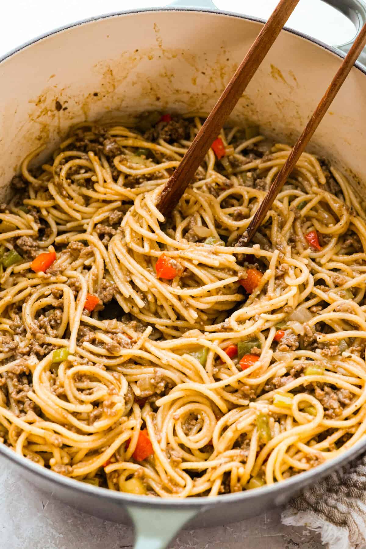 Move over spaghetti and meat sauce, dirty spaghetti is here to spice up dinner! Inspired by Cajun dirty rice, it's a one-pot recipe loaded with seasoned beef, tender vegetables, and bold flavors in every bite. Pot of dirty spaghetti being stired with wooden tongs.