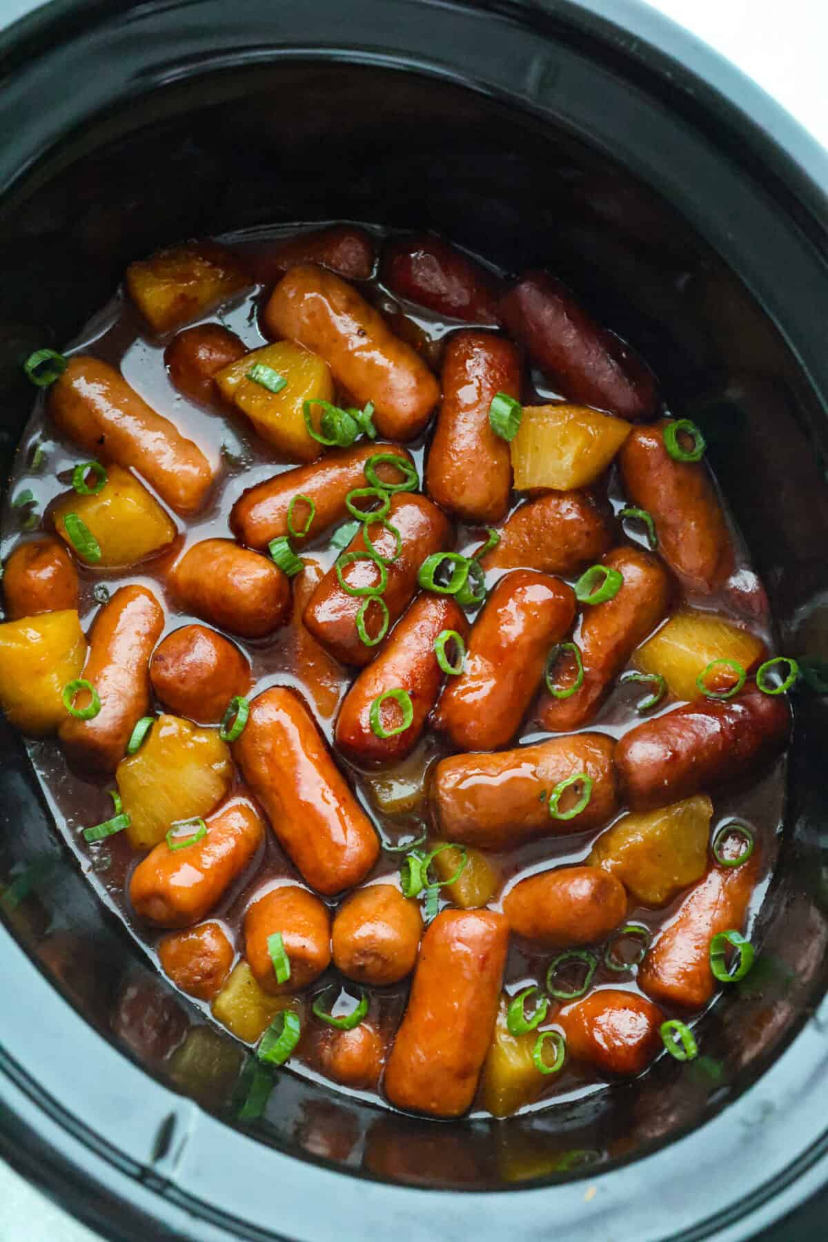 Don't be surprised if these Hawaiian Lil' Smokies steal the show! Slow cooked in a sweet and tangy pineapple BBQ sauce, they're bite-sized, irresistible, and dangerously easy to snack on. Overhead shot of the hawaiian little smokies in a slow cooker.