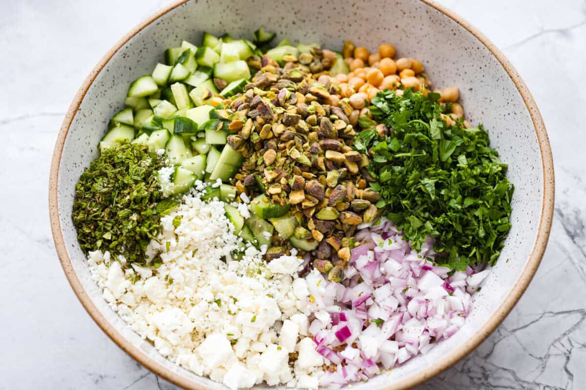 This Jennifer Aniston Salad is light, fresh, and perfect for summer lunches. Itโs packed with veggies, chickpeas, herbs, pistachios, and feta, then tossed in a simple lemon dressing that makes everything taste bright and delicious. All of the ingredients added to a large bowl.