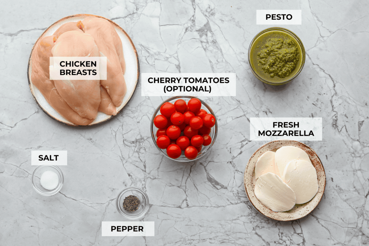 This pesto chicken is the kind of dinner you can assemble right in the baking dish and let the oven take it from there. Add the chicken, pesto, mozzarella, and tomatoes to one pan, bake until tender and bubbly, and dinner is done. Overhead shot of labeled baked pesto chicken ingredients.