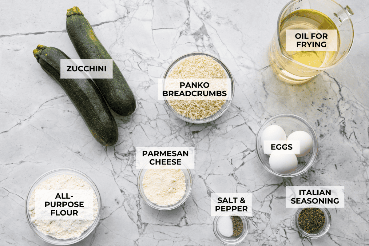 When my garden is overflowing with zucchini, this crispy Parmesan fried zucchini is one of my favorite things to make. It’s ready in just 15 minutes and is perfect as a quick appetizer, snack, or easy side with ranch, marinara, or fry sauce. Overhead shot of labeled fried zucchini ingredients.