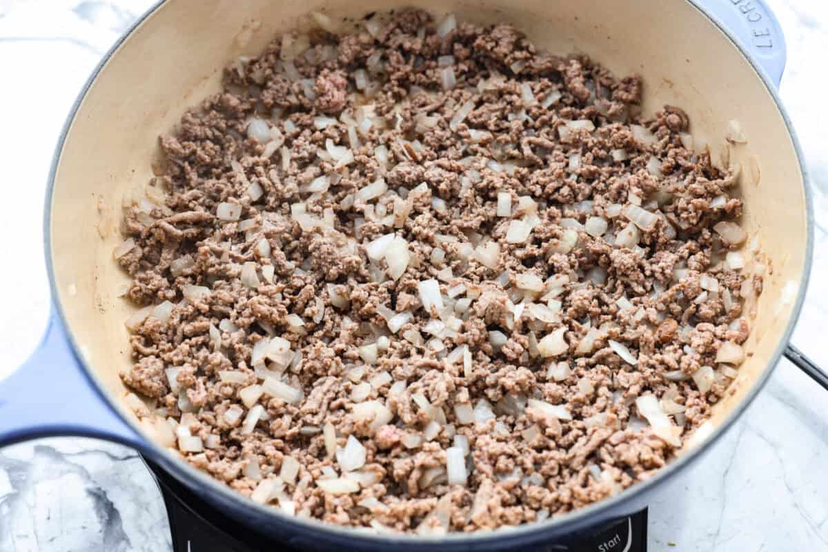If your family loves tacos and mac and cheese, this one pan taco mac is about to become a weeknight favorite! It's cheesy, hearty, packed with Tex-Mex flavor, and comes together in one skillet in just 30 minutes. Brown beef and onions cooking in a skillet.