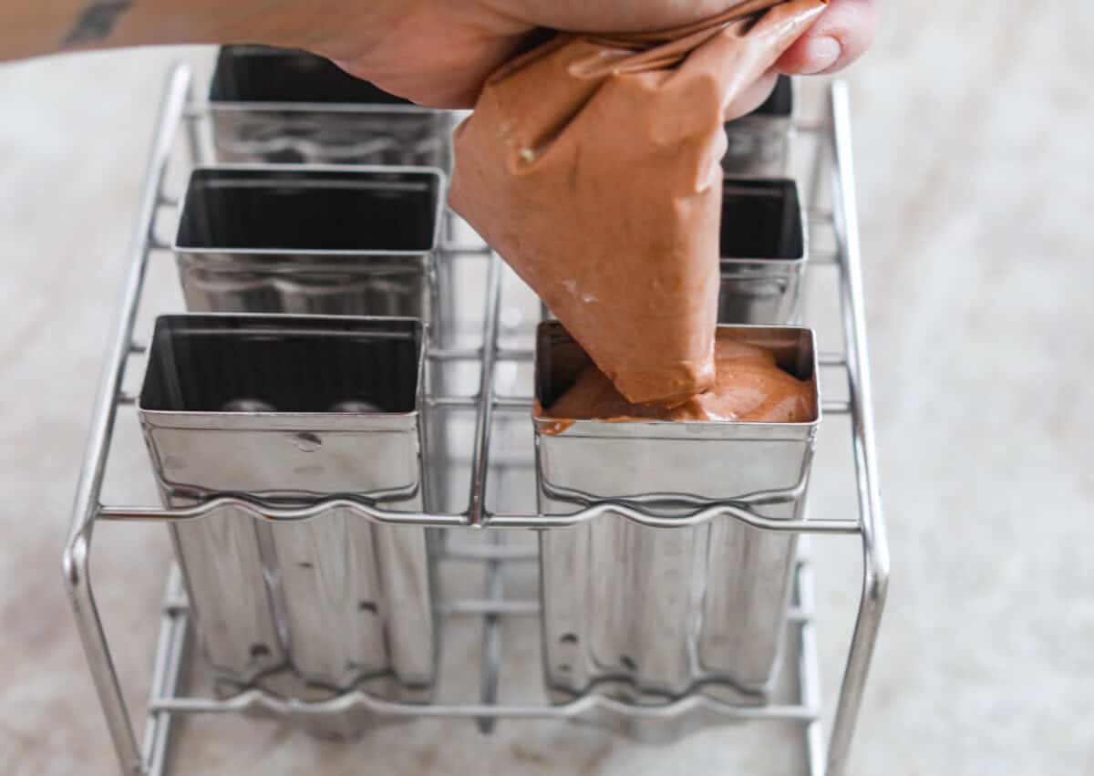 Someone squeezing the pudding mixture into the popsicle molds.