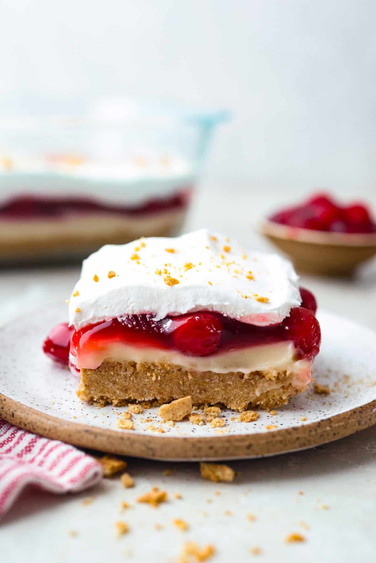 My cherry cheesecake lush is rich, creamy, and incredibly easy to make. With simple layers of graham cracker crust, cheesecake filling, juicy cherries, and whipped topping, it's the perfect no-bake dessert for any occasion. Side shot of a slice of cherry cheesecake lush.