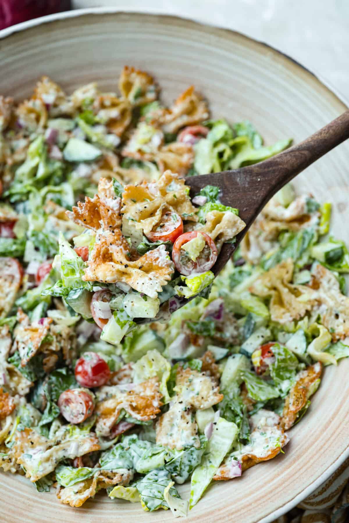 Large spoon lifting a scoop of crispy pasta salad out of the large serving bowl.