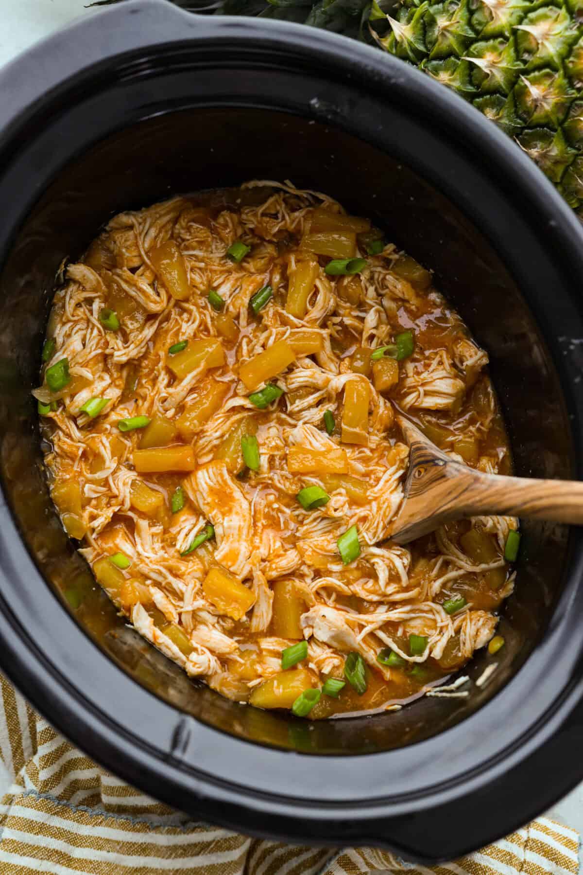 Crockpot full of tender slow cooker aloha chicken with pineapple and green onions. 