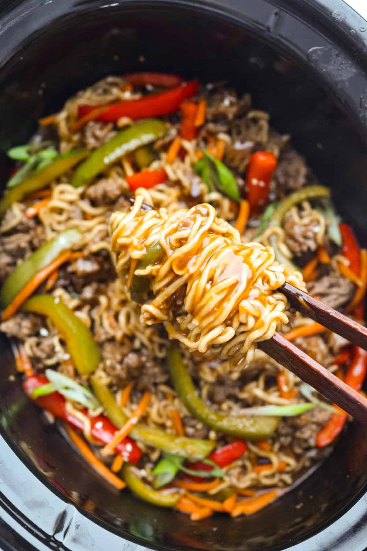 Slow cooker ramen gives you all the slurpy, saucy noodle bowl flavor with almost no effort. The veggies and beef slow cook in just an hour, then the ramen noodles go in for a quick 10 minutes. No hot oven, no boiling pots! Close up shot of the slow cooker ramen noodles being lifted up by chopsticks.