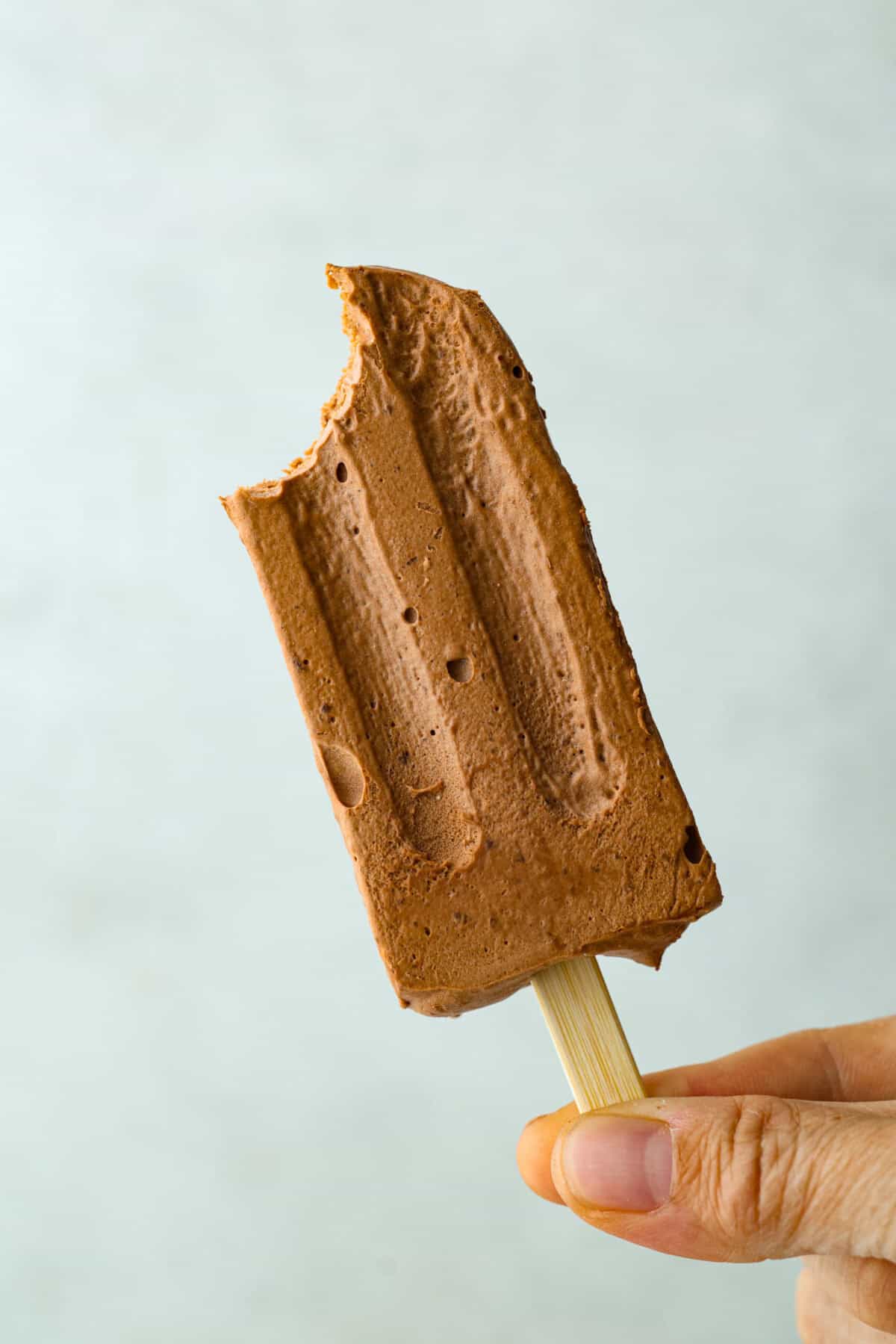 Someone holding up a pudding pop with a bite taken out of it. 