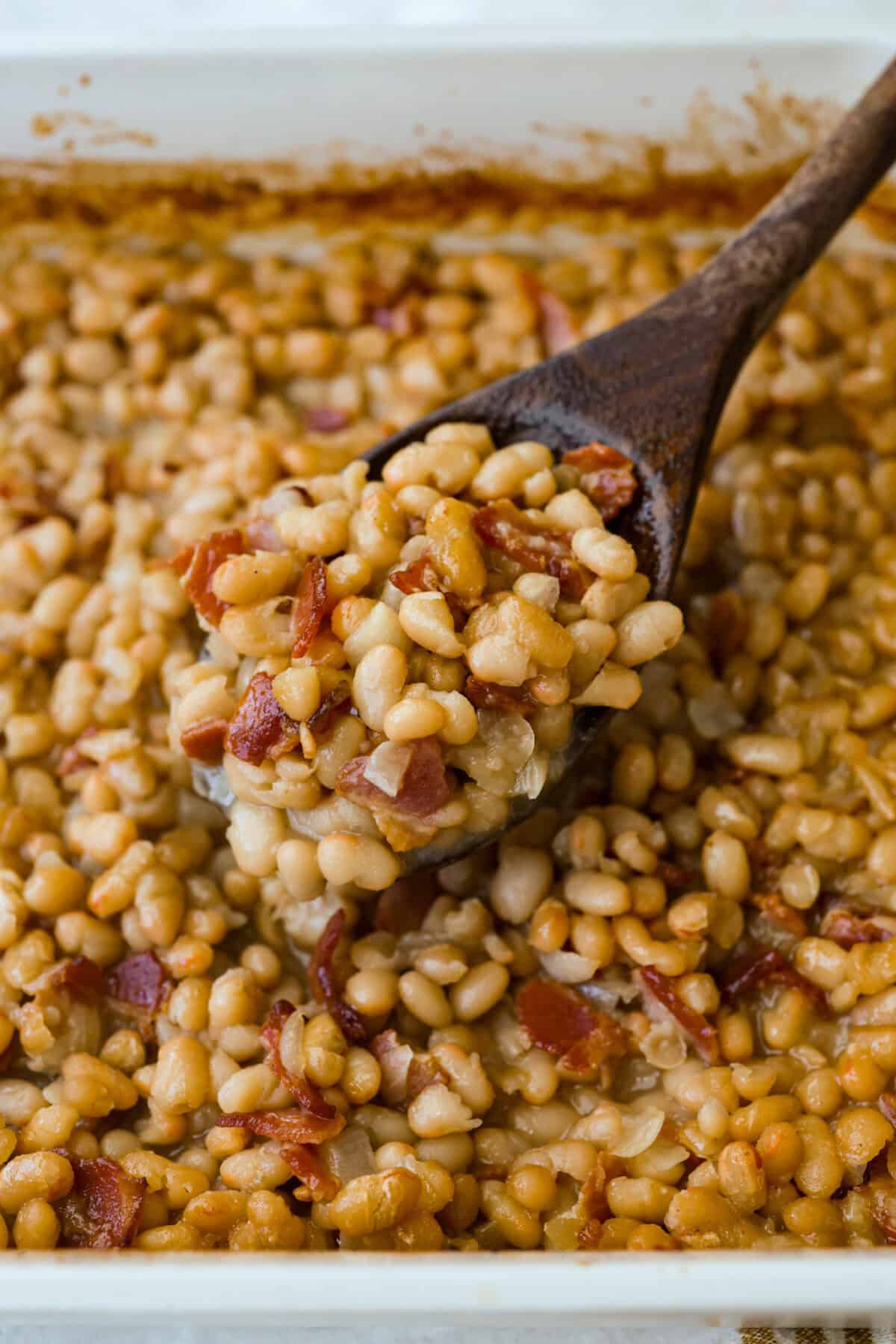 You're going to want this Copycat Grandma Brown’s Famous Baked Beans recipe in your life! It’s sweet, smoky, simple, and the perfect side dish for BBQs, summer cookouts, and every family get together. Someone lifting up a spoonful of the beans from the baking dish.
