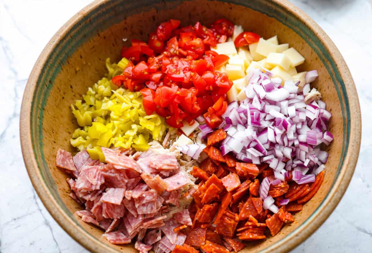 I know you guys love my famous grinder sliders. This grinder chicken salad brings all those bold flavors into one easy recipe. It's hearty, creamy, and perfect for lettuce wraps or a quick lunch straight from the bowl. Chicken salad ingredients added to a bowl.