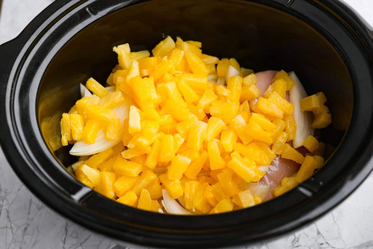 Slow cooker Aloha chicken is sweet, smoky, and so easy to throw together! Tender chicken cooks with pineapple, onion, and barbecue sauce until it’s full of flavor and ready to shred. Serve it over rice for a simple dinner the whole family will love. Pineapple and onion added to the crockpot.