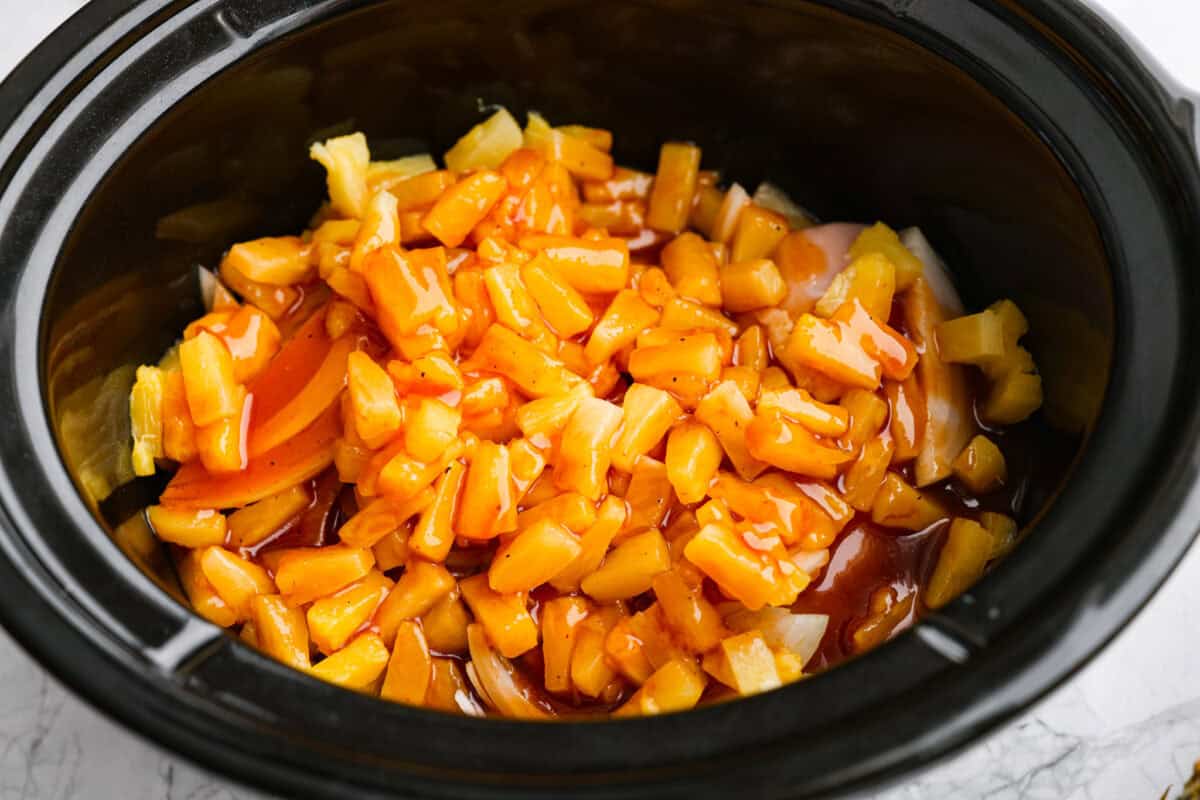 Slow cooker Aloha chicken is sweet, smoky, and so easy to throw together! Tender chicken cooks with pineapple, onion, and barbecue sauce until it’s full of flavor and ready to shred. Serve it over rice for a simple dinner the whole family will love. Sauce poured over the pineapple, onion, and chicken in the slow cooker.
