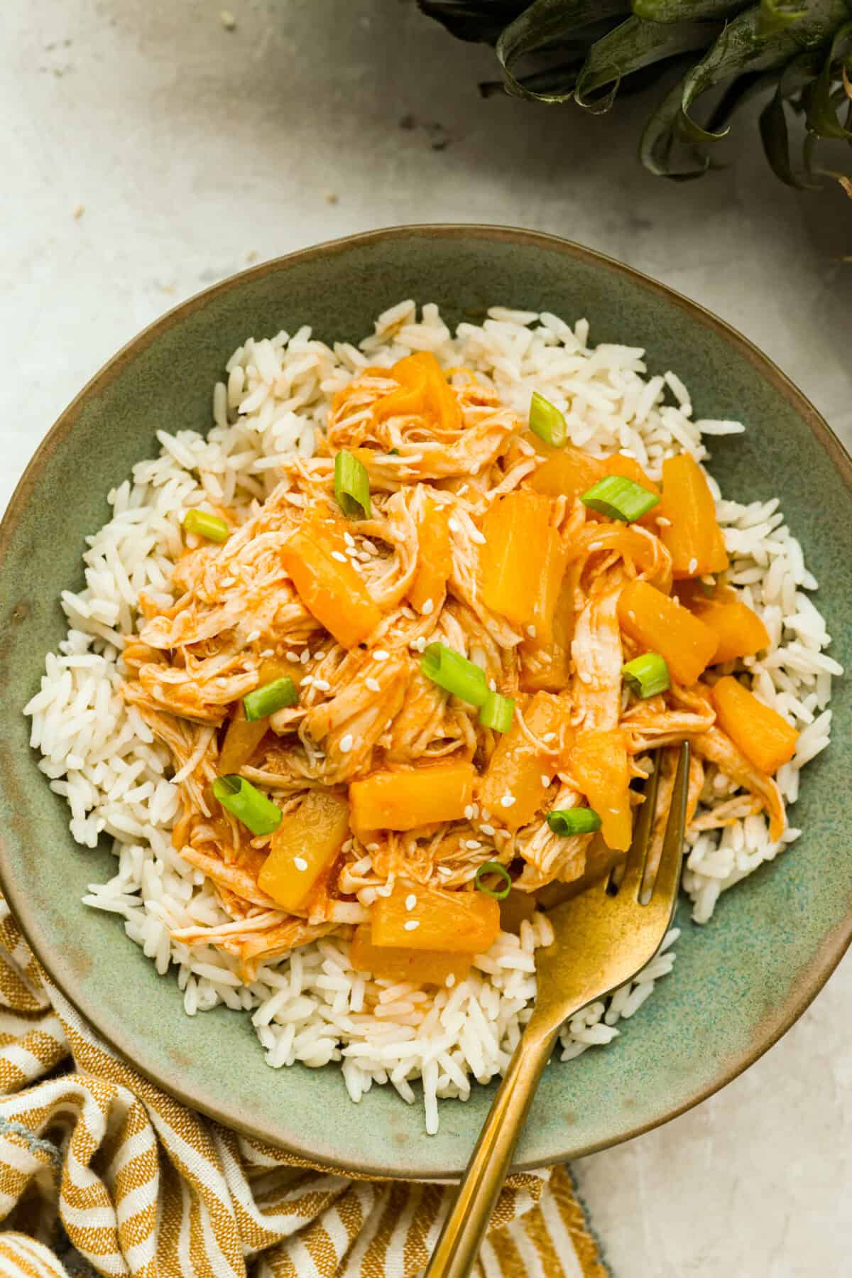 Slow cooker Aloha chicken is sweet, smoky, and so easy to throw together! Tender chicken cooks with pineapple, onion, and barbecue sauce until it’s full of flavor and ready to shred. Serve it over rice for a simple dinner the whole family will love. Plated slow cooker aloha chicken on a bed of rice.