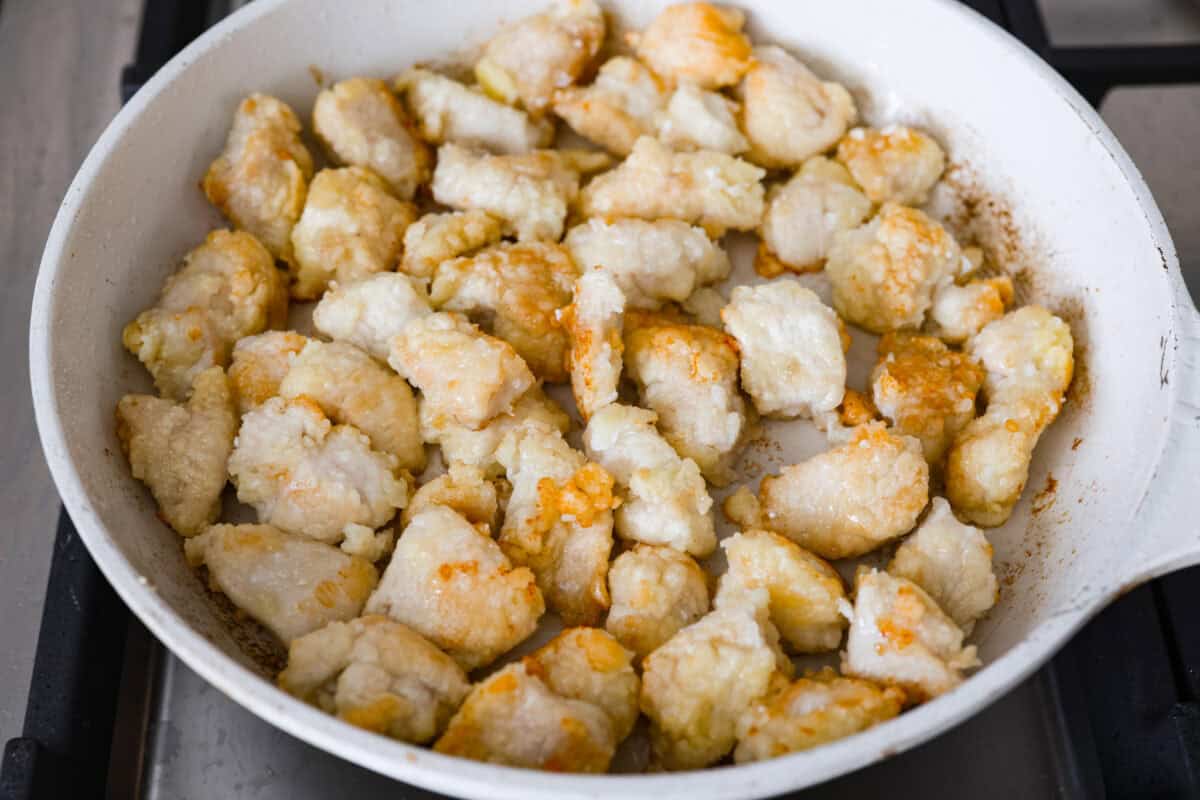 Sticky apricot chicken is crispy, saucy, and loaded with sweet and savory flavor. Golden chicken pieces are tossed in a glossy apricot sauce with garlic, ginger, soy sauce, and a touch of chili paste. Ready in just 30 minutes! Coated chicken pieces cooking in a skillet.