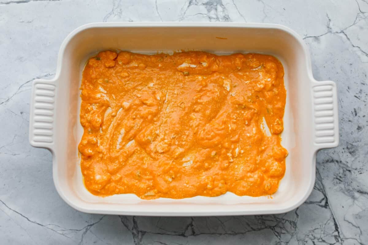 Take your lasagna night to the next level with this buffalo chicken lasagna! Every layer is packed with creamy buffalo sauce, tender shredded chicken, and plenty of melty cheese for a fun twist on a comfort food classic. Part of the sauce spread across the bottom of the 9x13 baking dish.