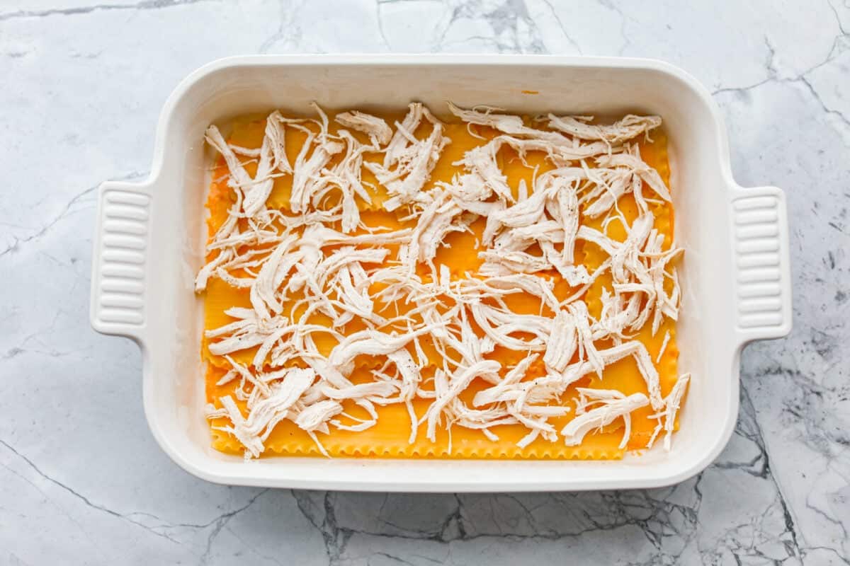 Take your lasagna night to the next level with this buffalo chicken lasagna! Every layer is packed with creamy buffalo sauce, tender shredded chicken, and plenty of melty cheese for a fun twist on a comfort food classic. Shredded cooked chicken spread out over the noodles.