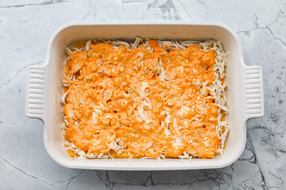 Take your lasagna night to the next level with this buffalo chicken lasagna! Every layer is packed with creamy buffalo sauce, tender shredded chicken, and plenty of melty cheese for a fun twist on a comfort food classic. Sauce spread out over the chicken.