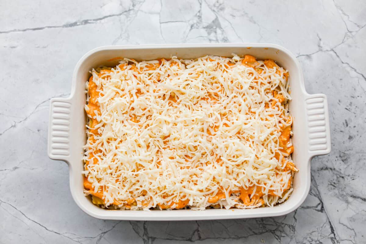 Take your lasagna night to the next level with this buffalo chicken lasagna! Every layer is packed with creamy buffalo sauce, tender shredded chicken, and plenty of melty cheese for a fun twist on a comfort food classic. Buffalo chicken lasagna all layered and ready to be cooked, topped with cheese.