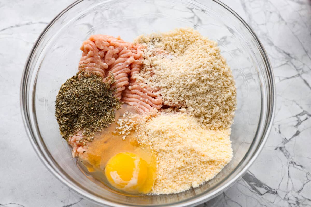 Chicken parmesan meatballs bring all the best parts of chicken parmesan together in one skillet. Think tender chicken meatballs, crispy Parmesan breadcrumbs, saucy marinara, and lots of melted mozzarella. Ground chicken, seasonings, egg, panko breadcrumbs, and parmesan cheese all added to a mixing bowl.