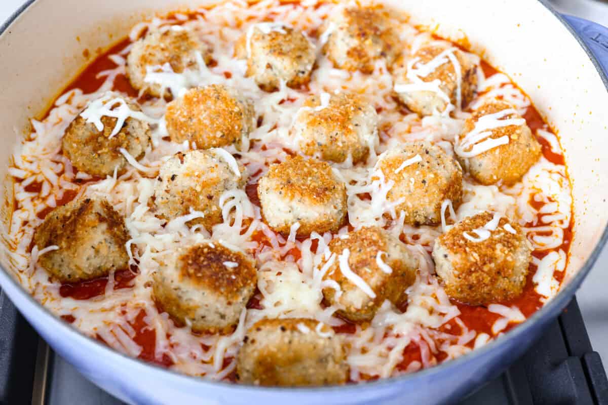 Chicken parmesan meatballs bring all the best parts of chicken parmesan together in one skillet. Think tender chicken meatballs, crispy Parmesan breadcrumbs, saucy marinara, and lots of melted mozzarella. Browned meatballs, marinara sauce and cheese added to the skillet ready to be baked in the oven.