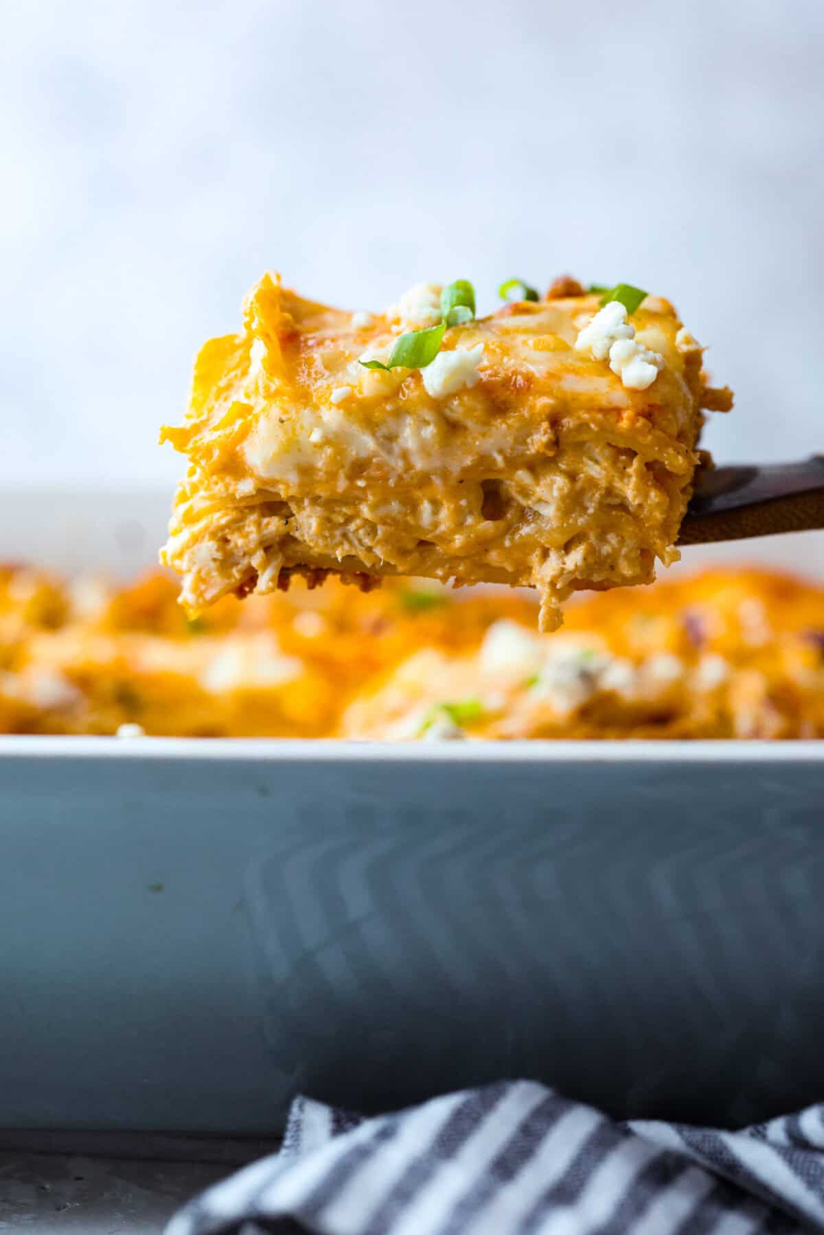 Take your lasagna night to the next level with this buffalo chicken lasagna! Every layer is packed with creamy buffalo sauce, tender shredded chicken, and plenty of melty cheese for a fun twist on a comfort food classic. Side shot of a slice of buffalo chicken lasagna being lifted out of the baking dish.