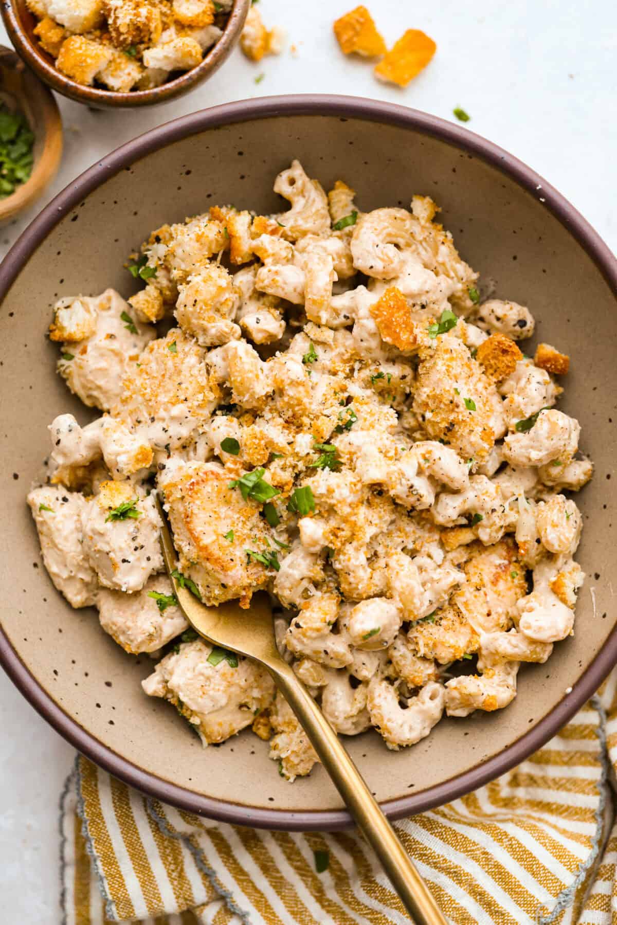 Chicken Caesar pasta is the kind of dinner you’ll want on repeat. You loved my Caesar Chicken Bake, so I turned those same creamy, savory flavors into an easy skillet pasta! It’s cozy, cheesy, and topped with crunchy croutons. Serving of chicken Caesar pasta in a bowl with a gold spoon.