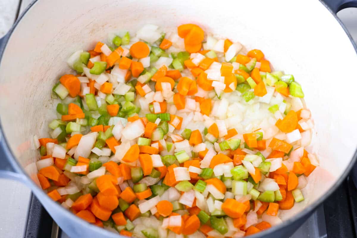 Chicken and dumpling soup will have everyone racing to the table! This one-pot dinner is loaded with tender chicken, hearty vegetables, and a creamy broth. Soft homemade dumplings steam right on top for the perfect finishing touch. Celery, onions, and carrots cooking in the olive oil in the pot.